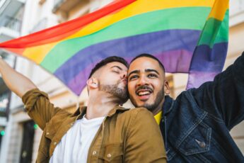 Gay couple embracing and showing their love with rainbow flag.