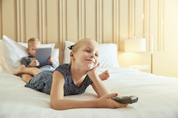 Smiling little girl watching television on a bed