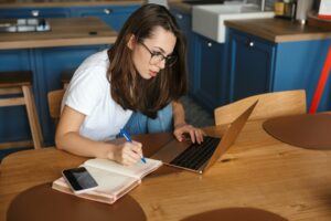 Image of serious nice woman working with laptop and writing