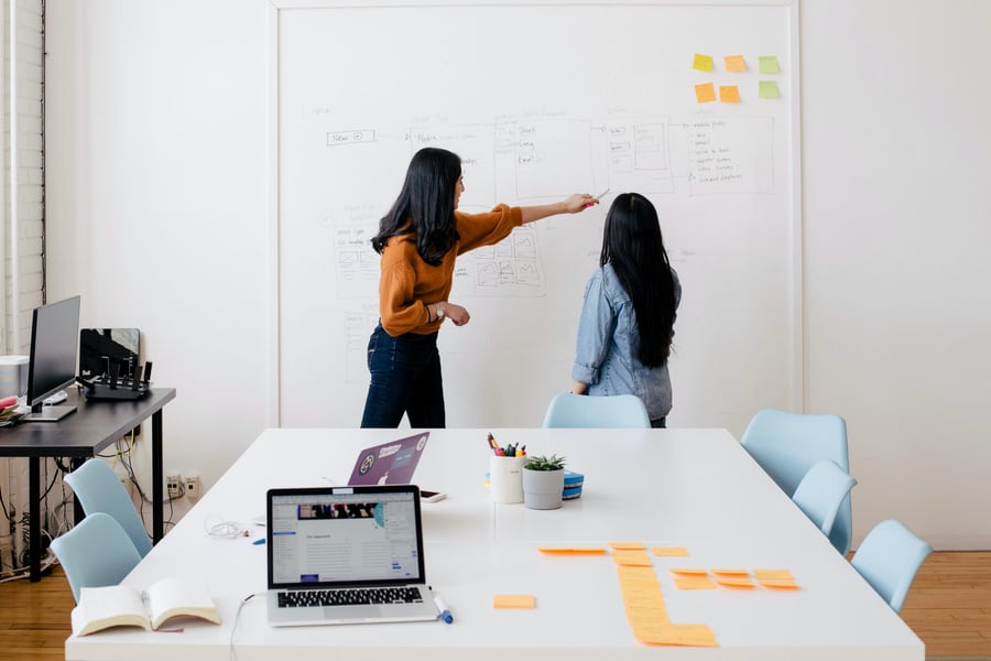 Two females with dark hair discuss tone and voice at a whiteboard.
