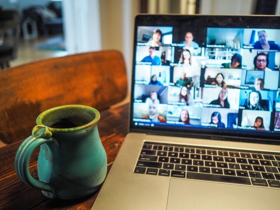 A green coffee mug rests next to a computer featuring a Zoom conference call.