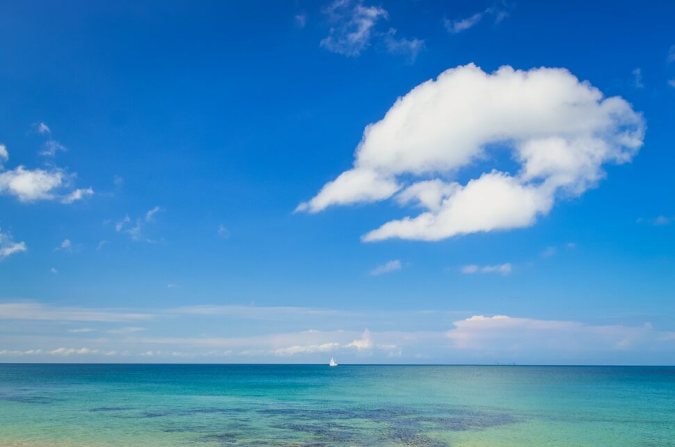 Ocean landscape with blue cloudy sky and sailboat