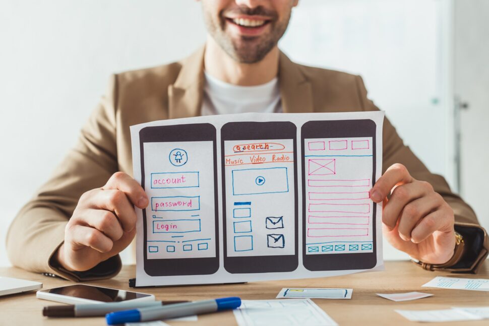 Cropped view of smiling designer showing mobile website wireframe sketches at table